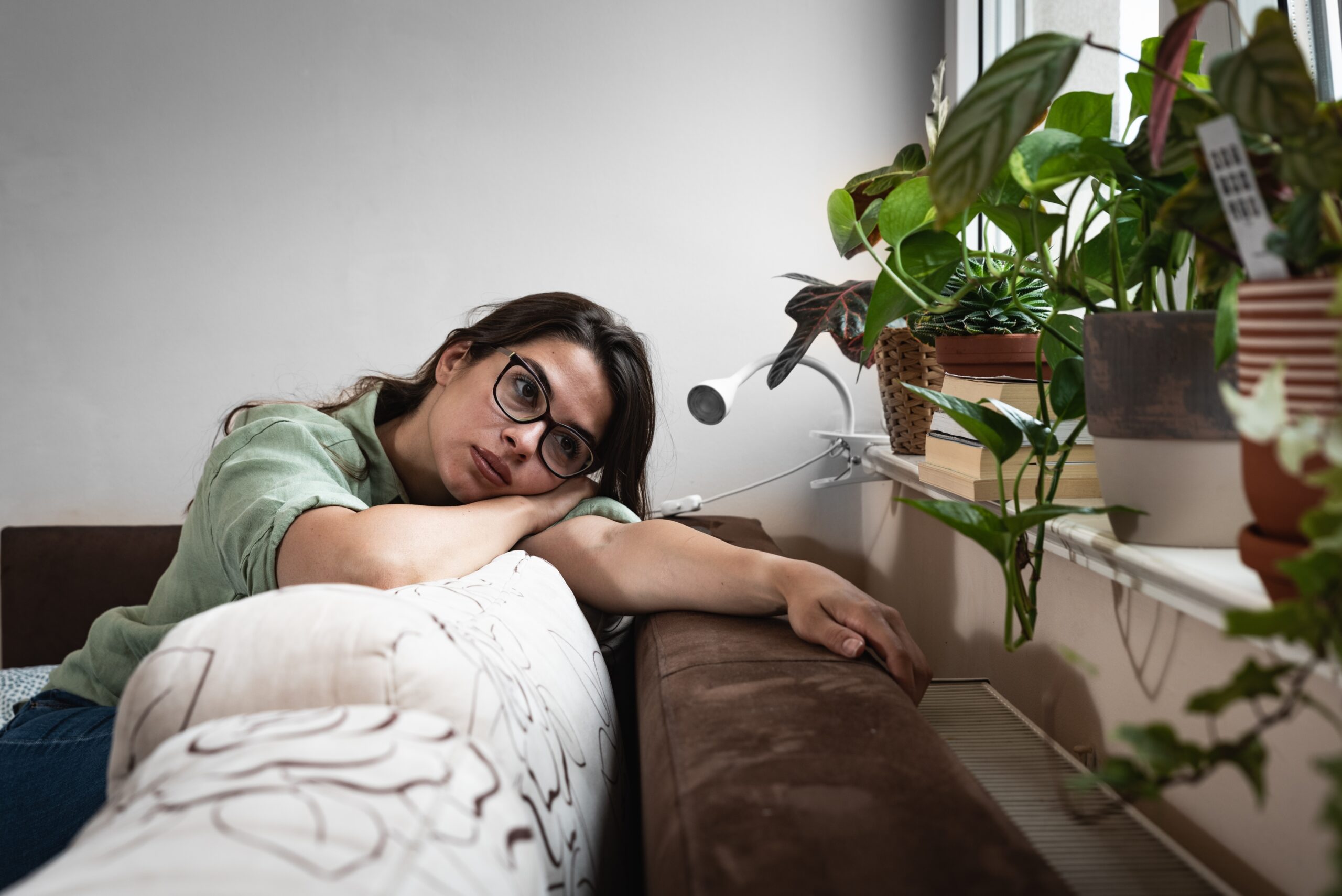 A woman lying on a couch, looking lost in thought—capturing the quiet struggle of overthinking before taking creative action.