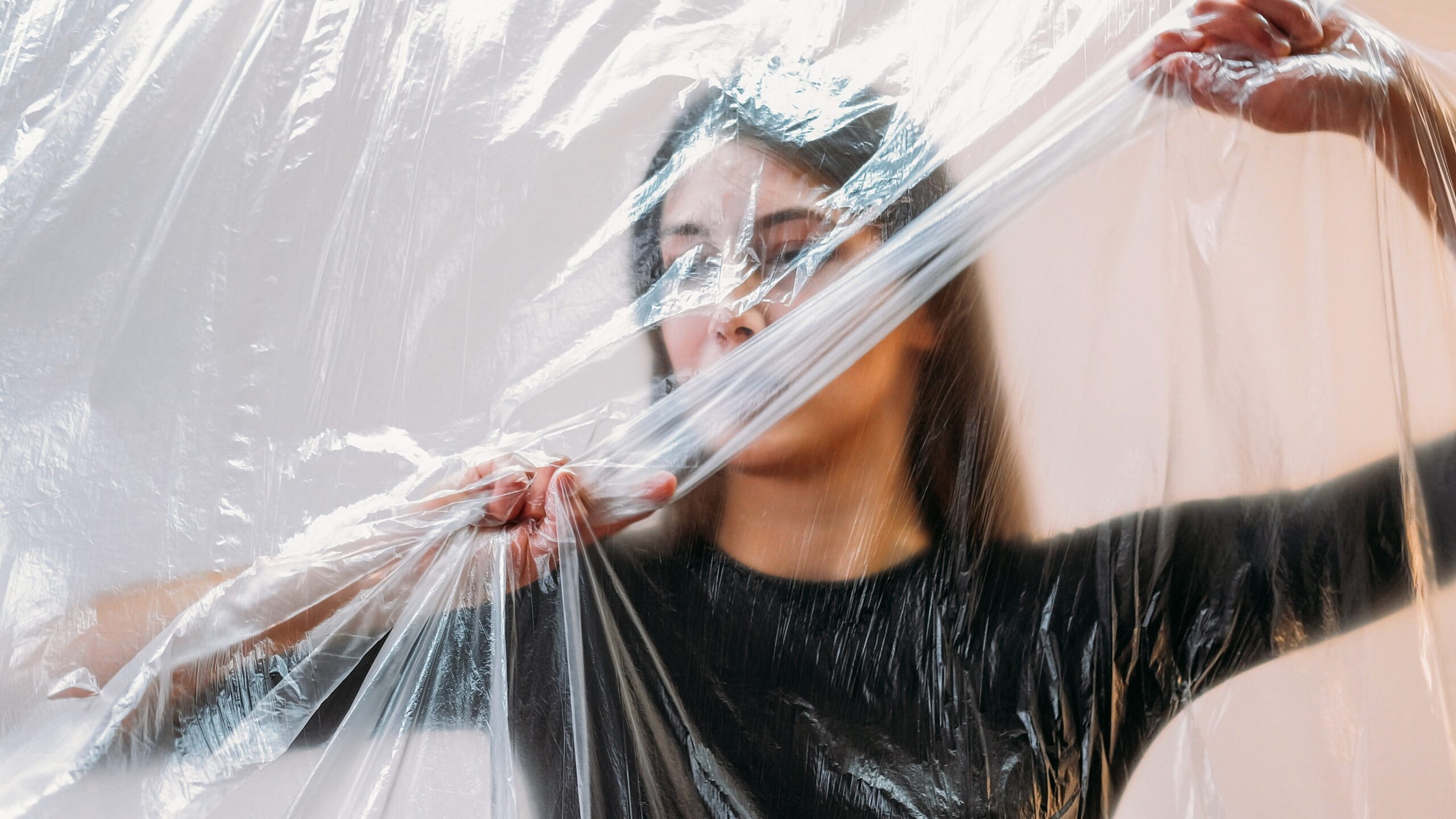 A woman pressing against a transparent plastic sheet—visually representing how creative constraints can shape expression and spark new ideas.