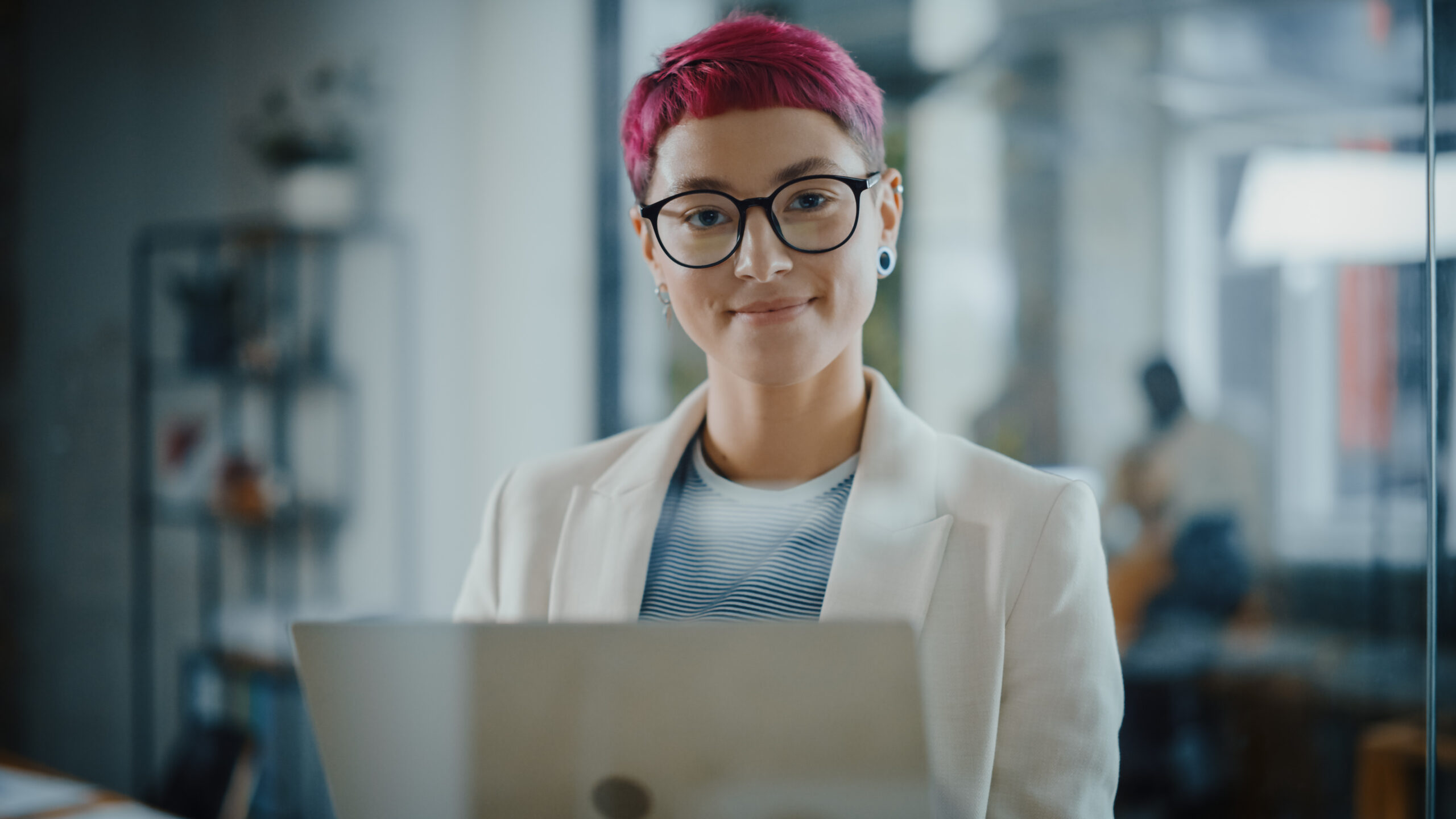 A confident person with vibrant pink hair and glasses smiling at the camera—capturing the moment of embracing and reclaiming a creative identity.